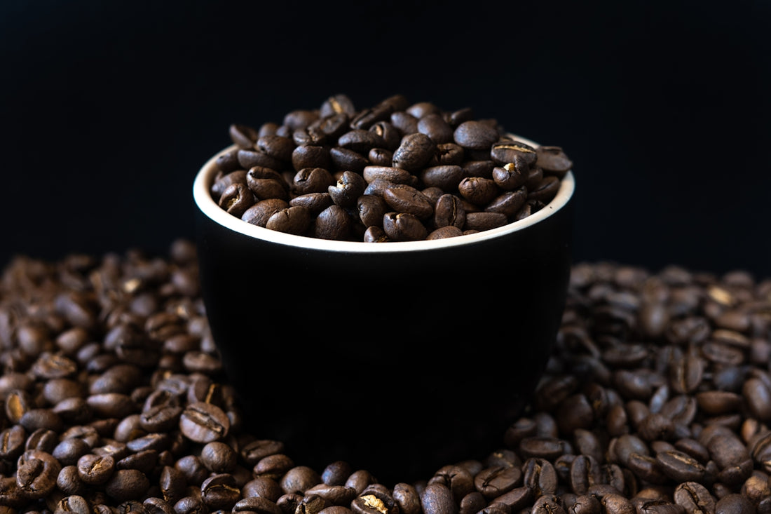 a black cup filled with coffee beans on top of a pile of coffee beans
