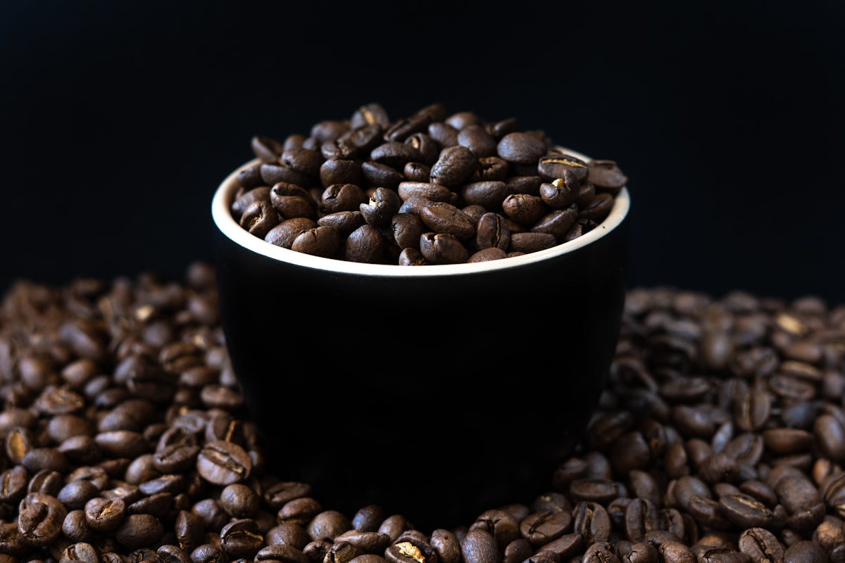 a black cup filled with coffee beans on top of a pile of coffee beans