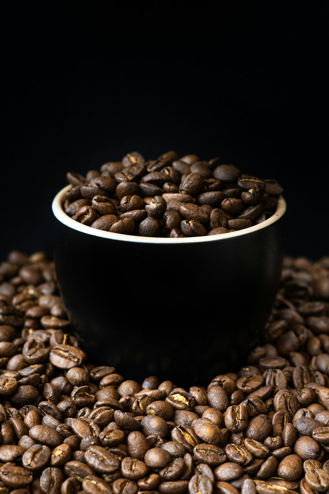 a black bowl filled with coffee beans on top of a pile of coffee beans