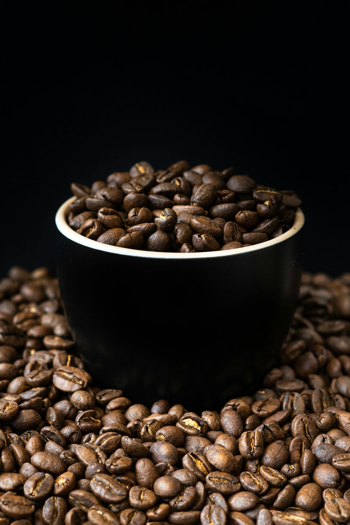 a black bowl filled with coffee beans on top of a pile of coffee beans